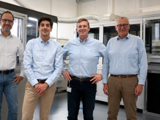 Four team members standing in a production facility, smiling, industrial machines in the background