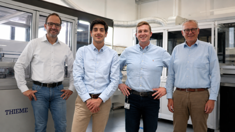 Four team members standing in a production facility, smiling, industrial machines in the background