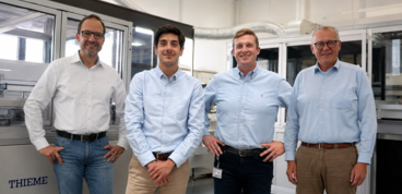 Four team members standing in a production facility, smiling, industrial machines in the background