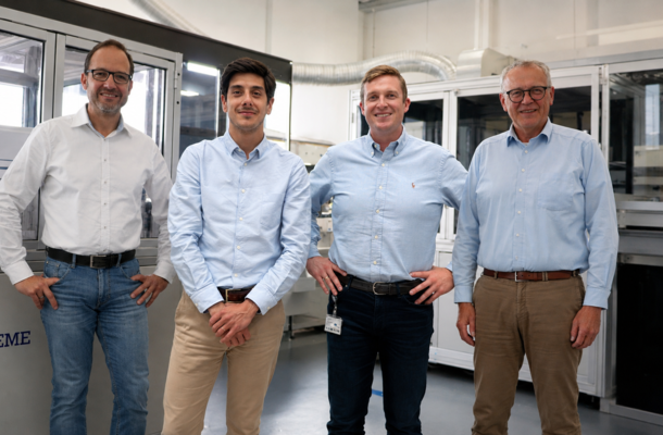 Four team members standing in a production facility, smiling, industrial machines in the background