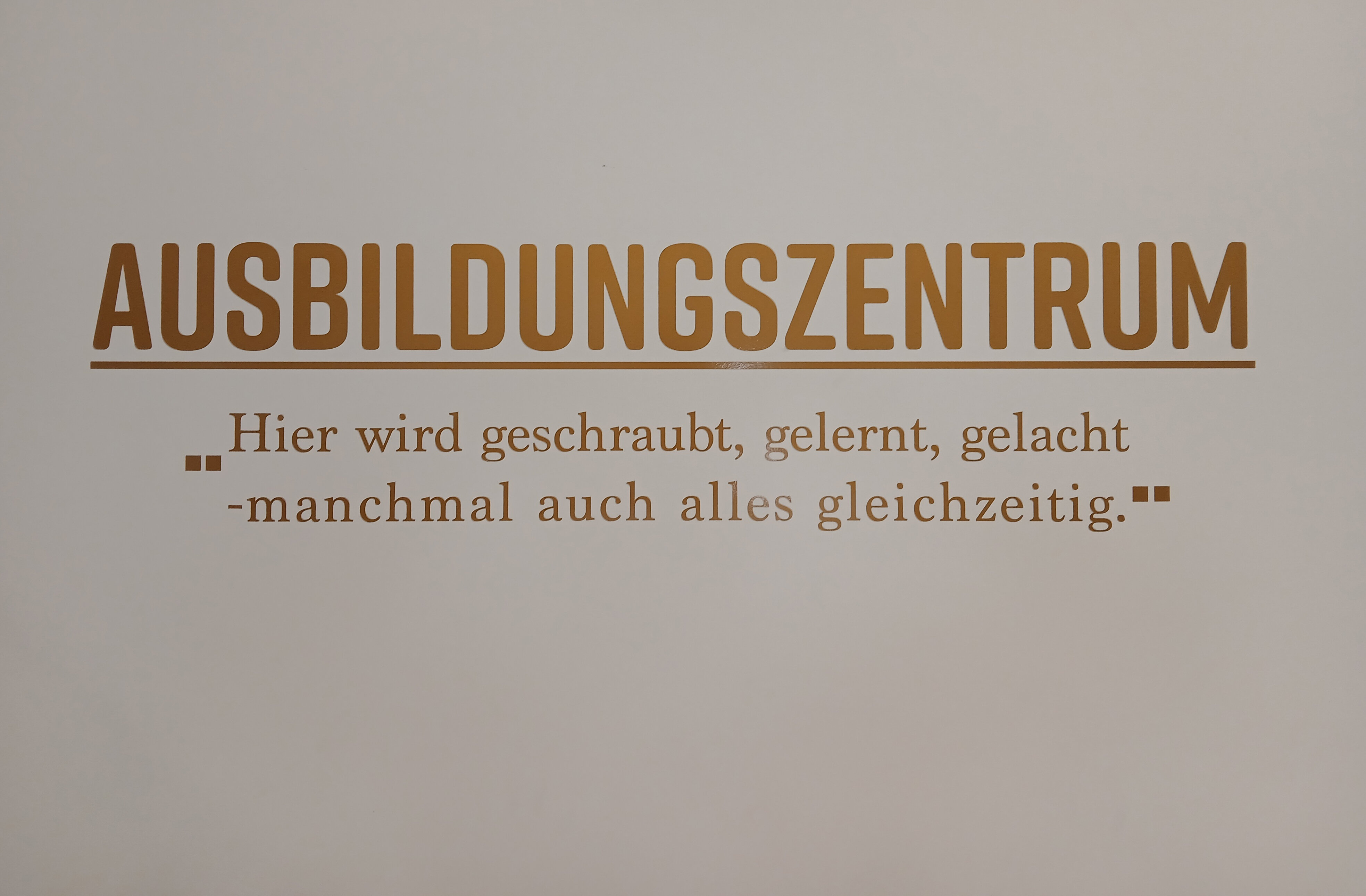 Wandaufschrift im Ausbildungszentrum mit dem Text: „Hier wird geschraubt, gelernt, gelacht – manchmal auch alles gleichzeitig.“